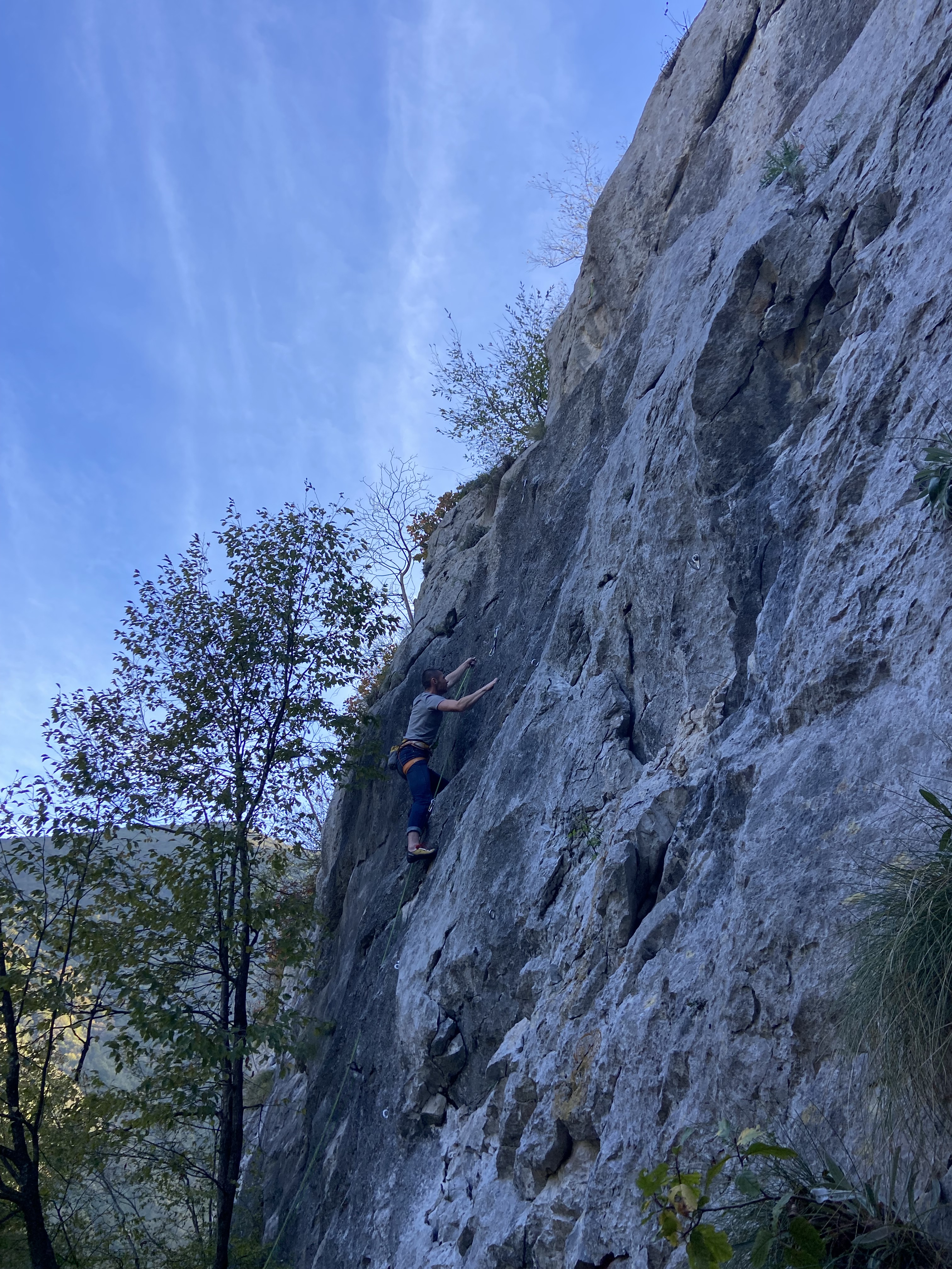 A climber about to clip a quickdraw on a slabby grey limestone cliff. 