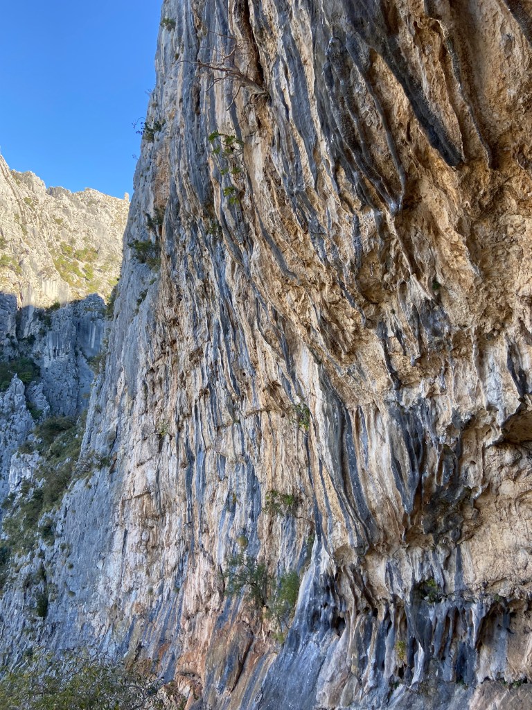 A big and imposing limestone cliff with lots of tufas and grey streaks among the predominately yellow rock. 