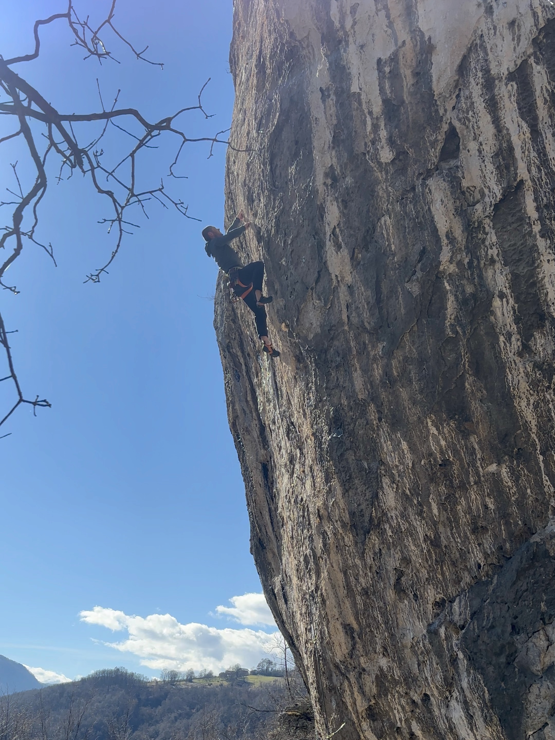 A climber in a grey fleece tackles a brutal pocketed headwall on sharp caramel coloured limestone. 